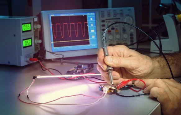 Engineer probing a circuit on an oscilloscope at a test bench