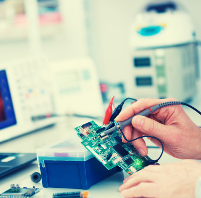 Engineer probing a circuit board on a test bench with an oscilloscope in the background